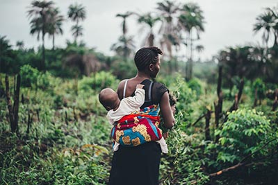 Person with baby on back in front of tropical landscape